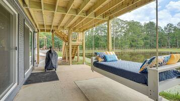 A covered outdoor seating area with a bed, a bench, and a view of a lake.