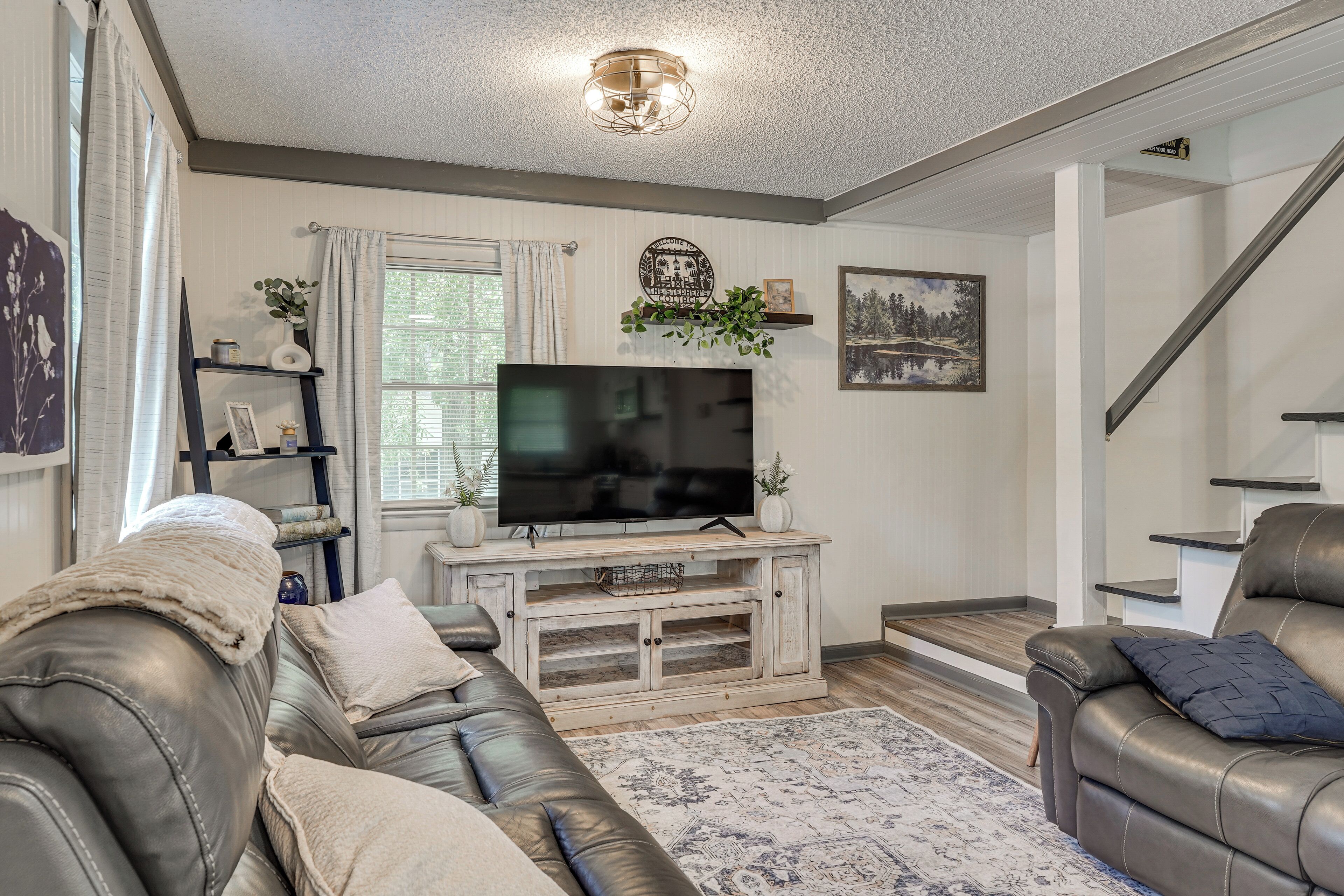 A living room with a flat-screen TV, leather sofas, a coffee table, and a staircase.