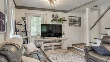 A living room with a flat-screen TV, leather sofas, a coffee table, and a staircase.