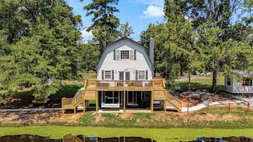 A two-story house with a balcony, a deck, and a pond in front.