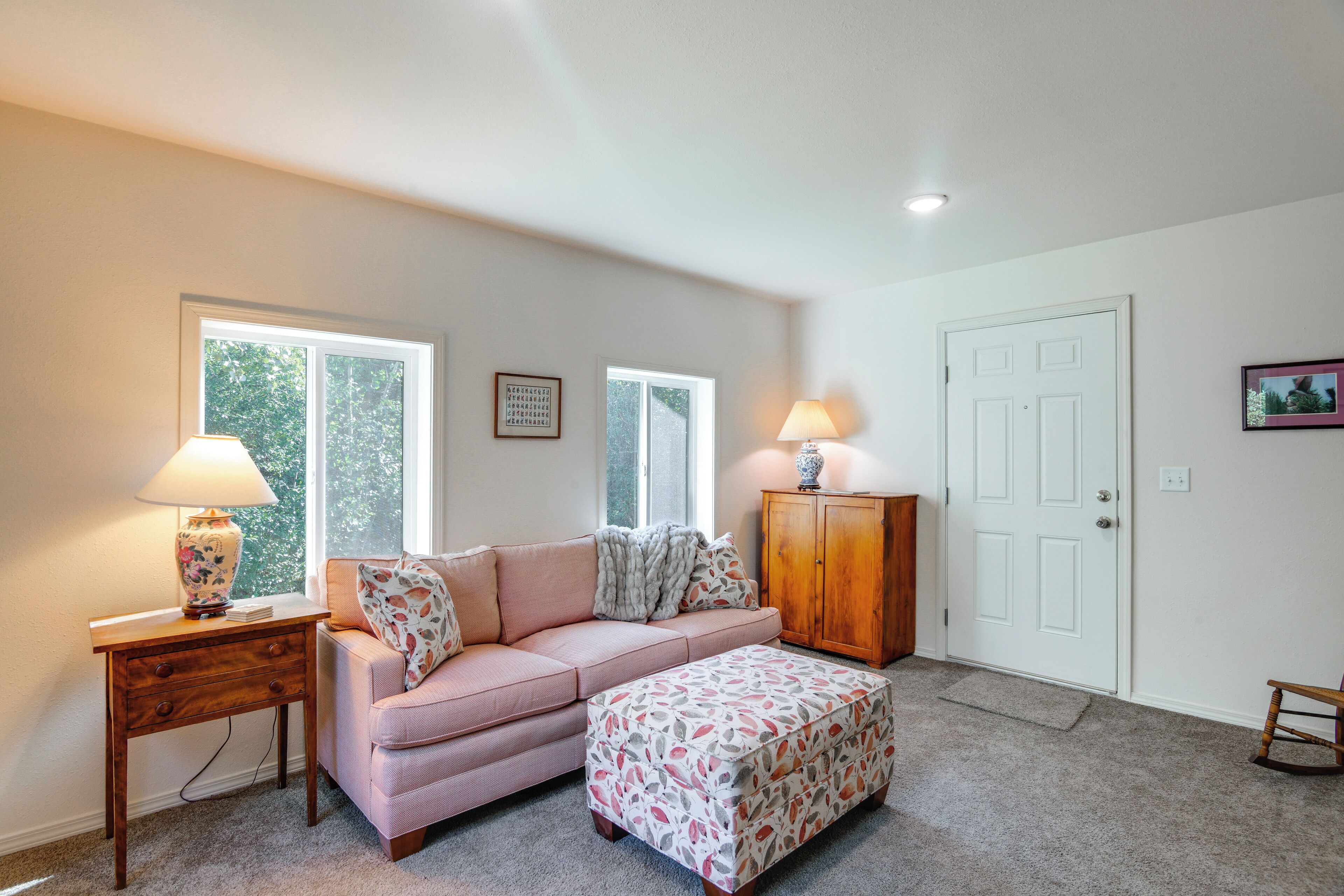 A room with a sofa, ottoman, two lamps, a cabinet, and a door.