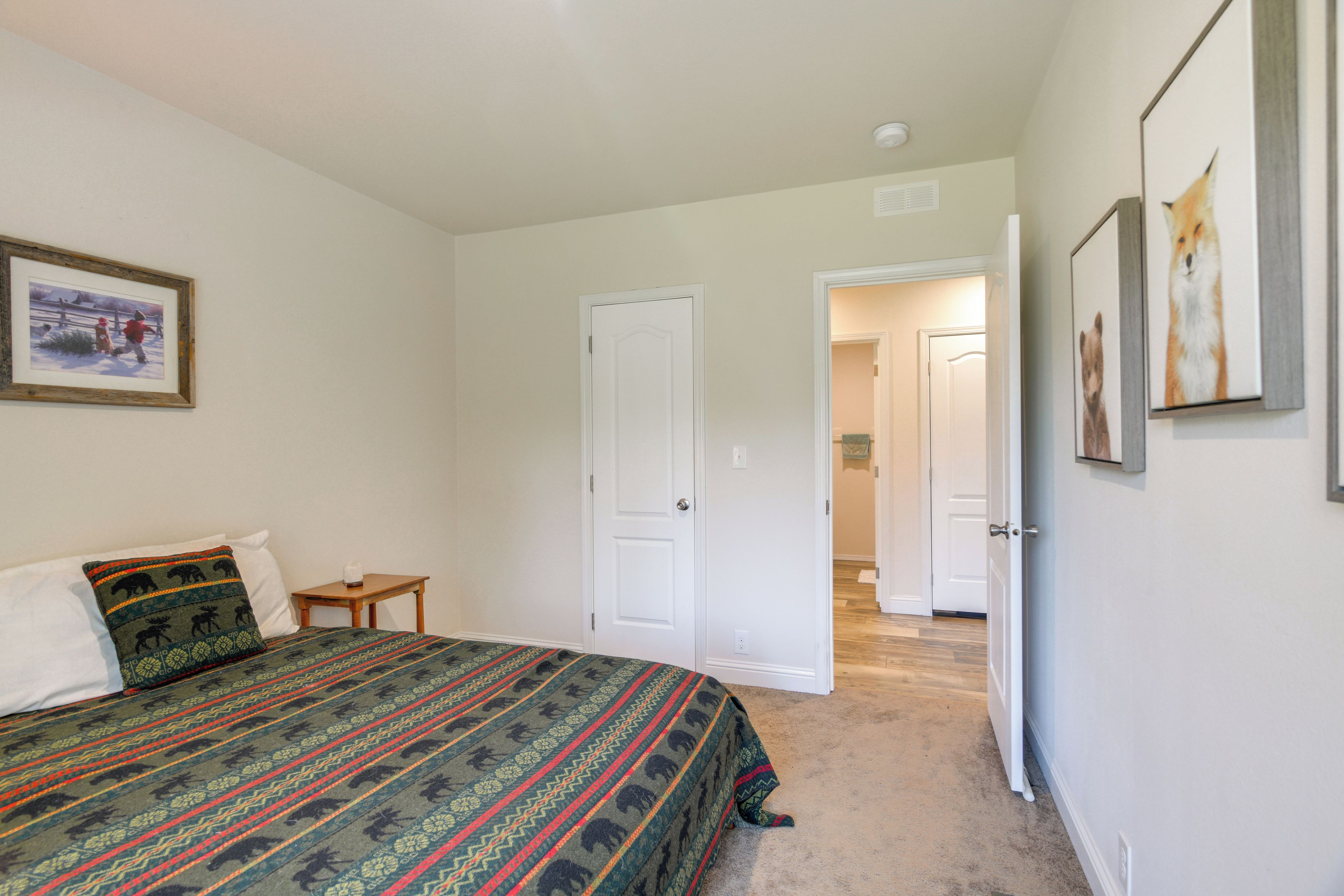 A bedroom with a bed, a nightstand, a door, and a hallway leading to another room.