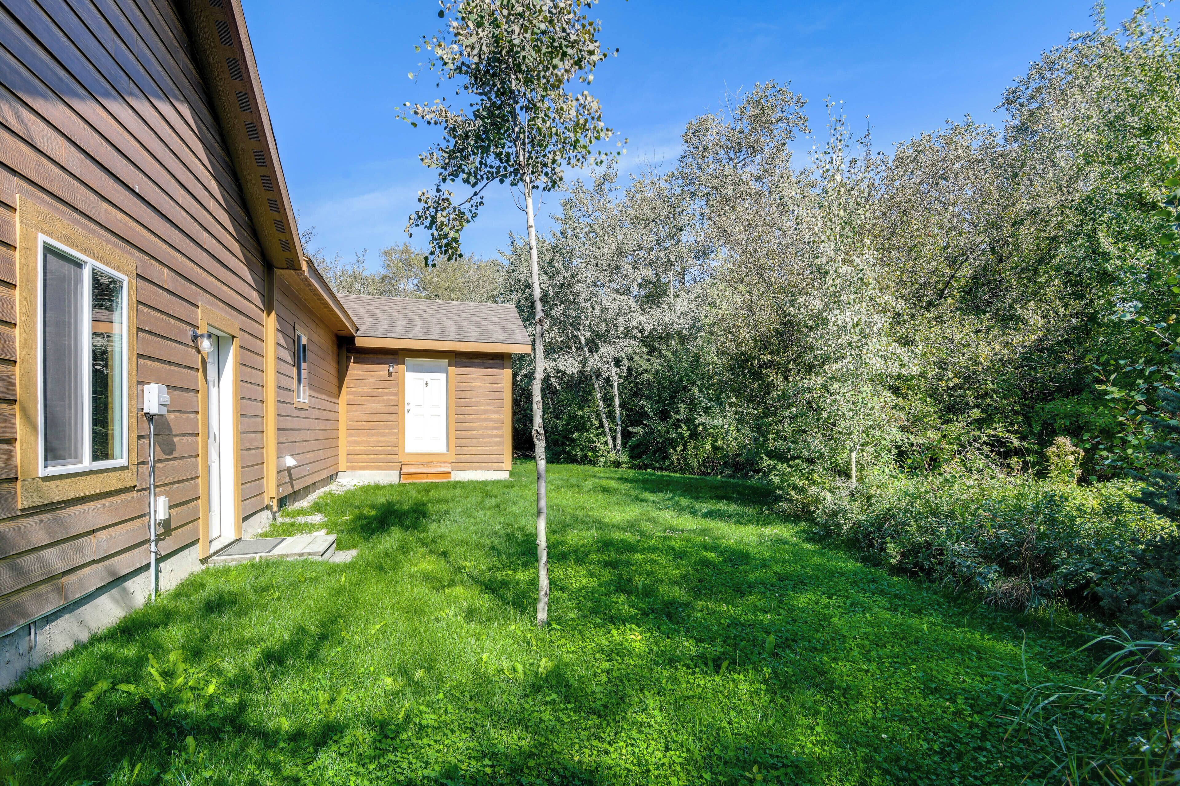 Une maison en bois avec un petit jardin devant et un arbre au centre.