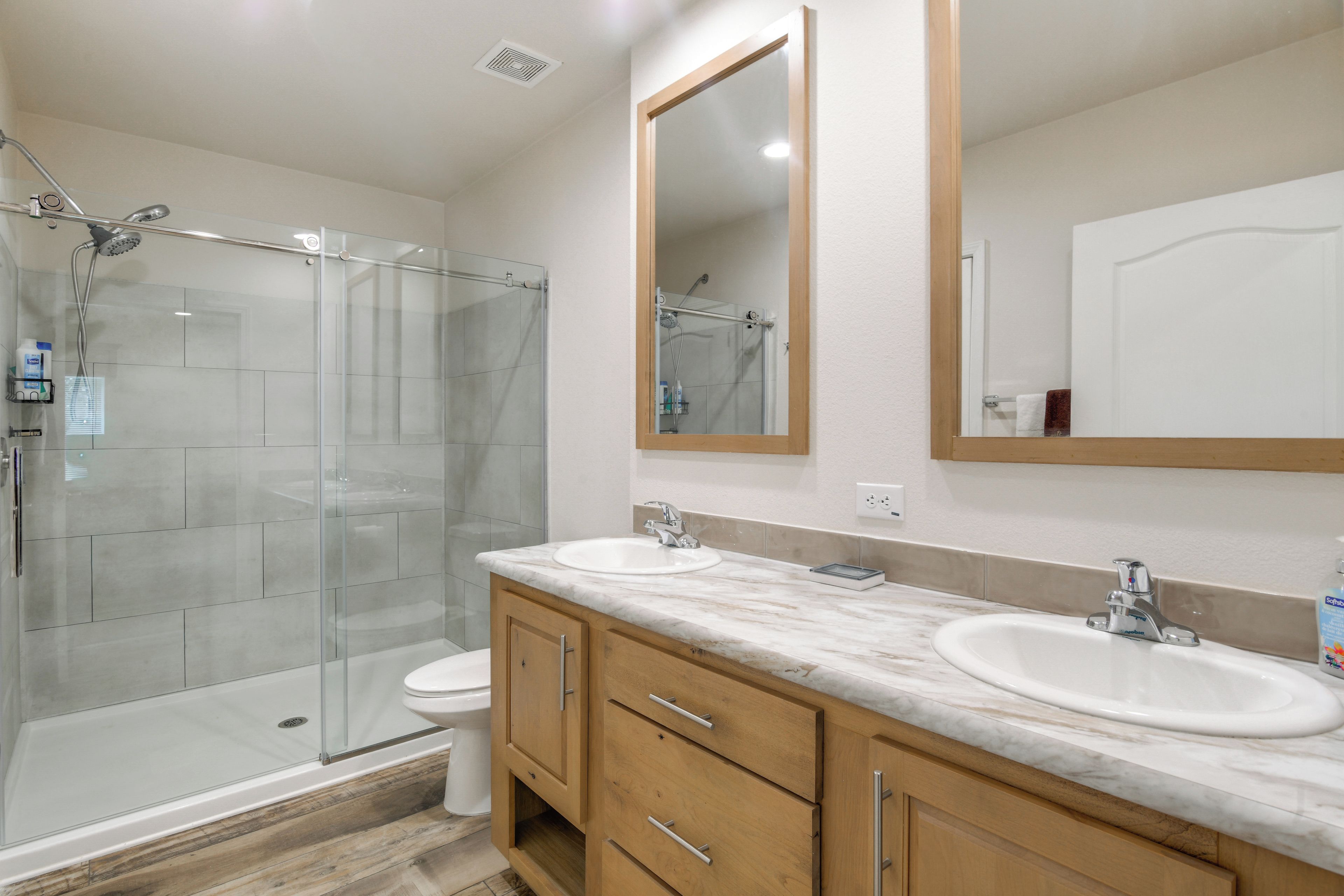 Une salle de bain avec une douche à parois de verre, deux lavabos et des meubles en bois.