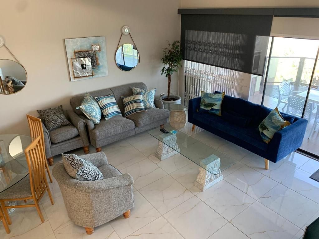 Una sala de estar con sofá, sillón, mesa de centro y un comedor con sillas y una mesa de vidrio.