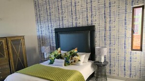 A hotel room with a bed, a nightstand, a lamp, and a patterned wall. - The Dolphines Hive View (iLembe District Municipality)