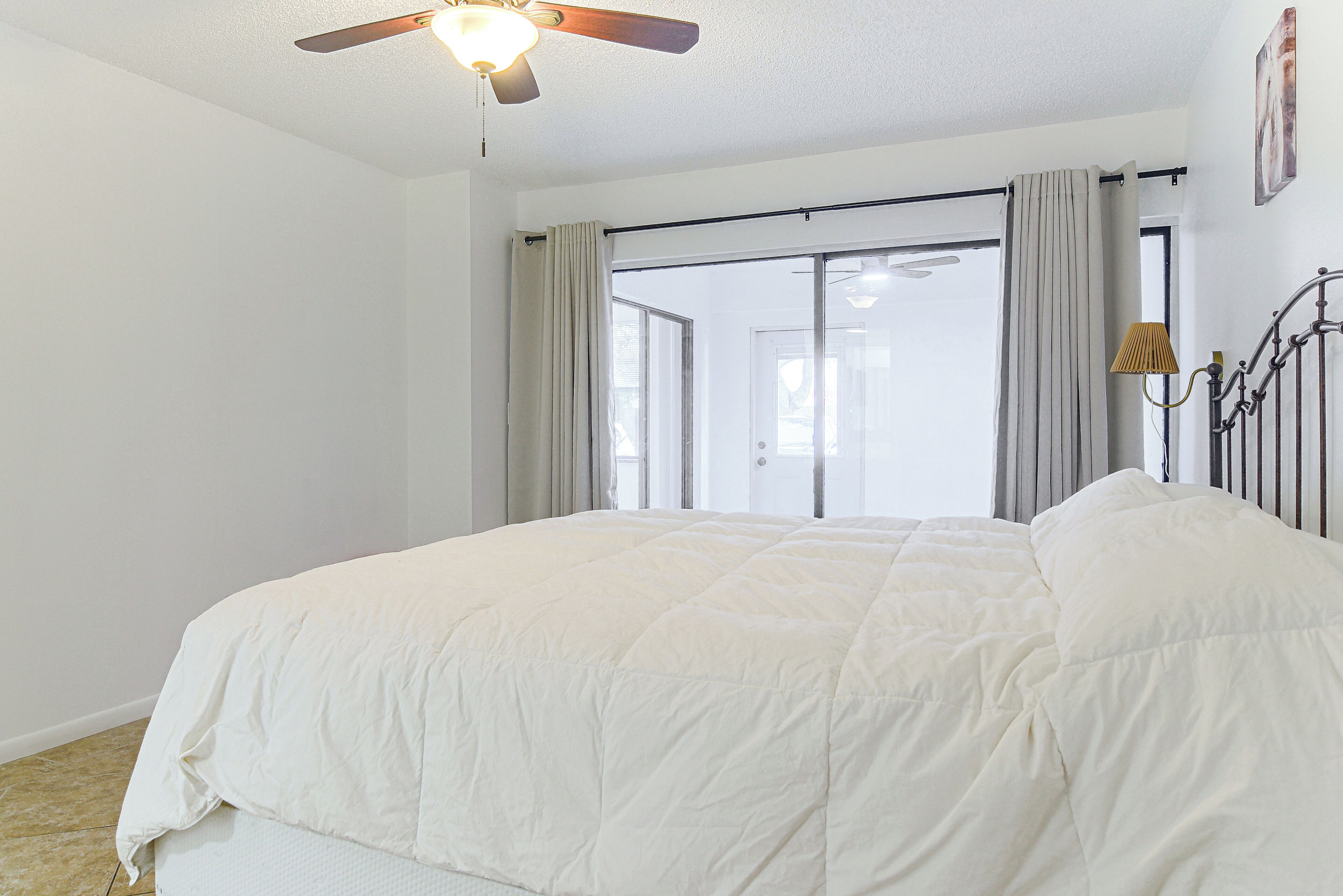 Un dormitorio con una cama grande, un ventilador de techo y vistas al exterior a través de una puerta corrediza.