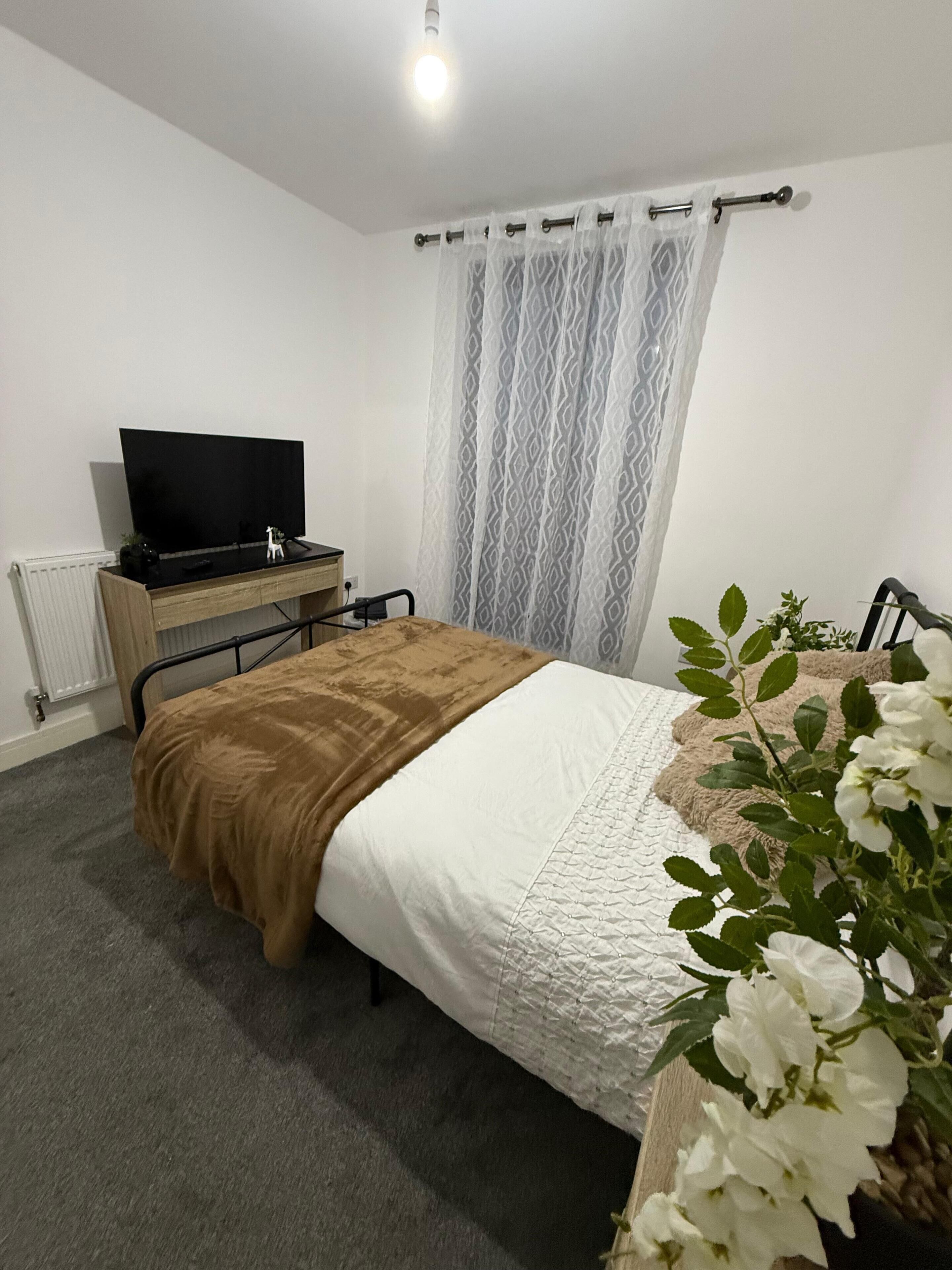 Ein Schlafzimmer mit einem Bett, einem Fernseher auf einem Holztisch, einem Heizkörper und einem Fenster mit Vorhängen.