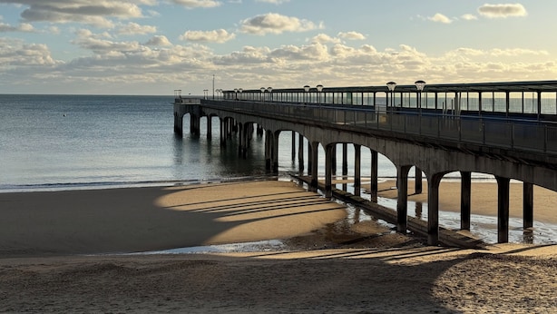 Eine Pier, die sich in ruhiges Wasser erstreckt, mit einem wolkenlosen Himmel darüber.