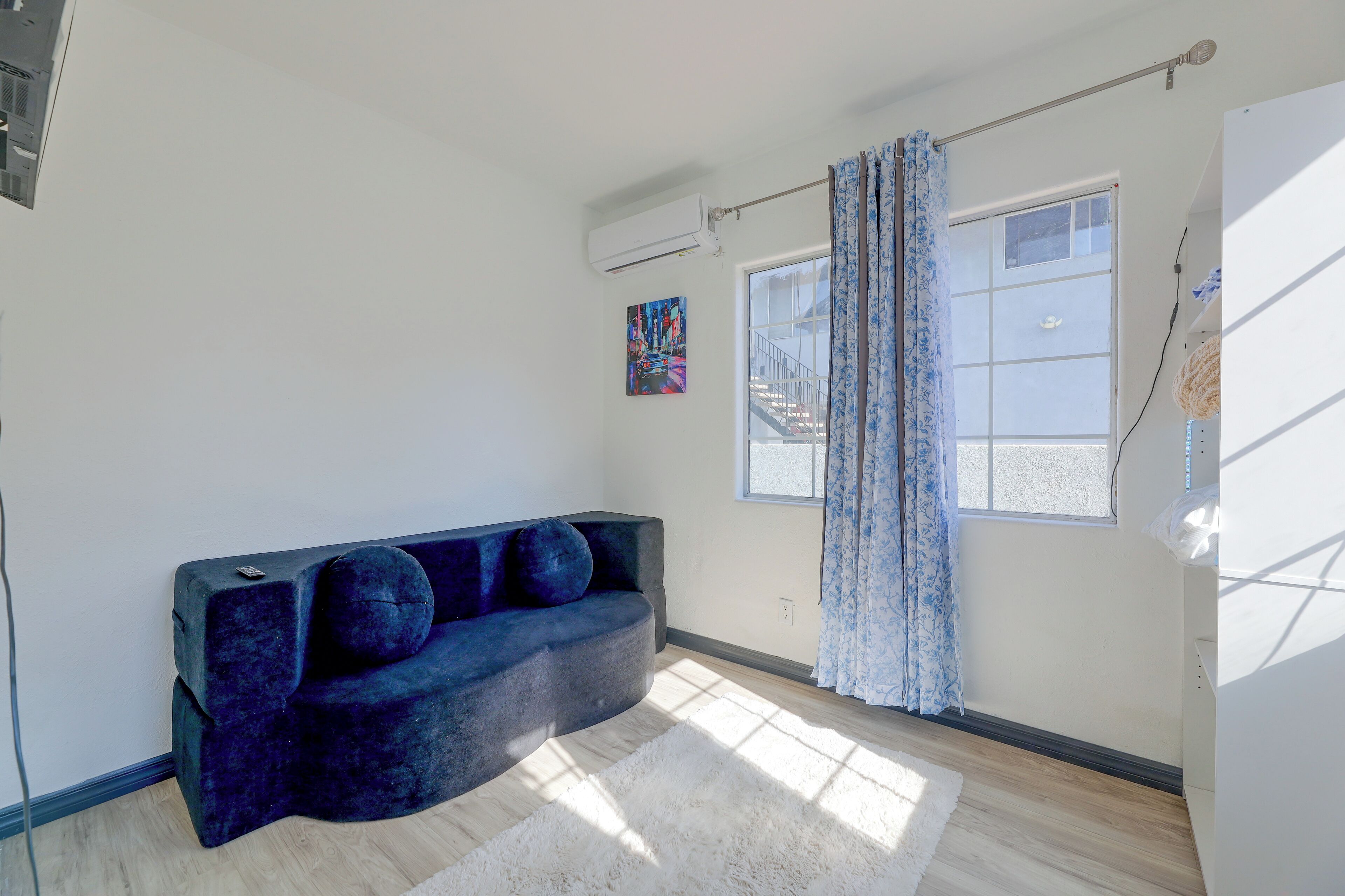 A modern living room with a dark blue sofa, a white rug, and a large window with blue curtains.