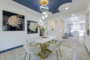 A modern dining area with a white table, gold chairs, and a decorative vase with flowers. - Walkable Location! Spacious Huntington Park Home (Huntington Park)