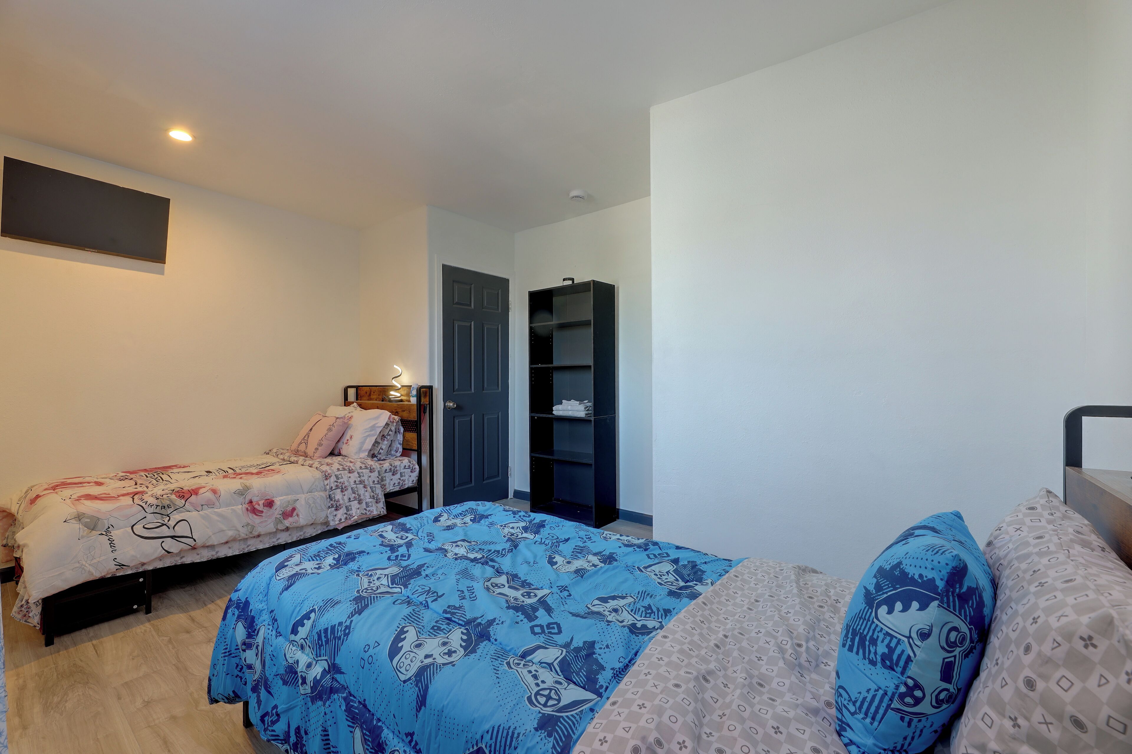 A bedroom with two beds, a wardrobe, and a shelf unit.