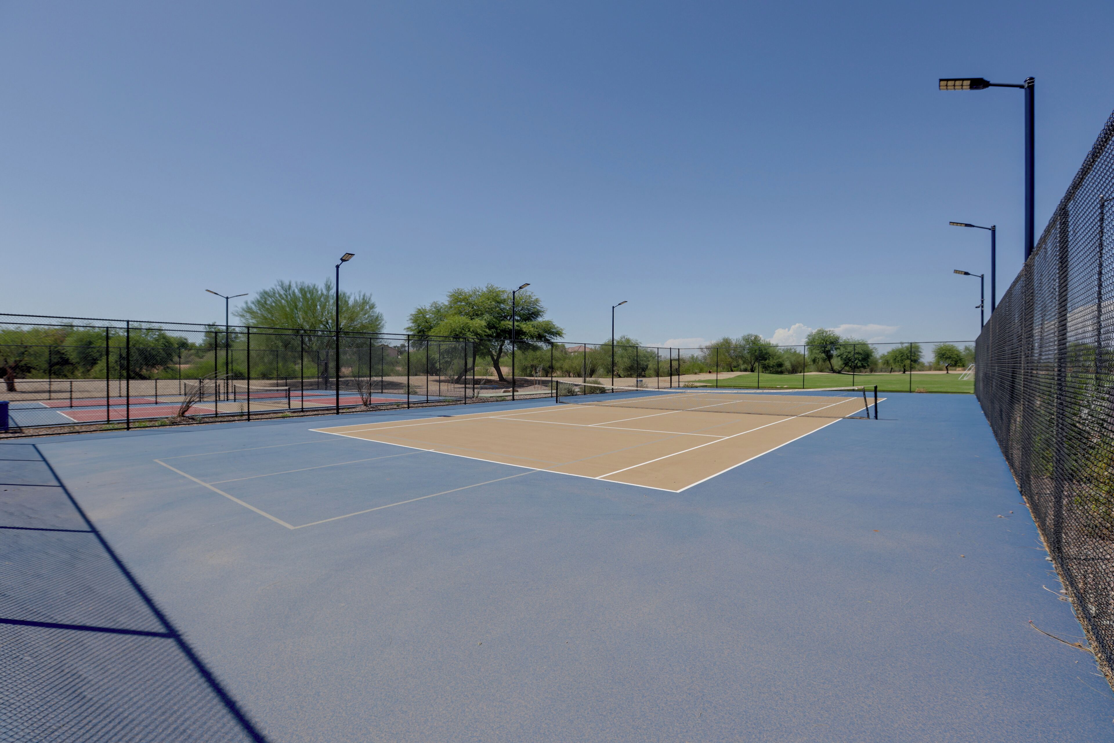 Ein Tennisplatz mit Netz, umzäunt und mit Straßenlaternen.