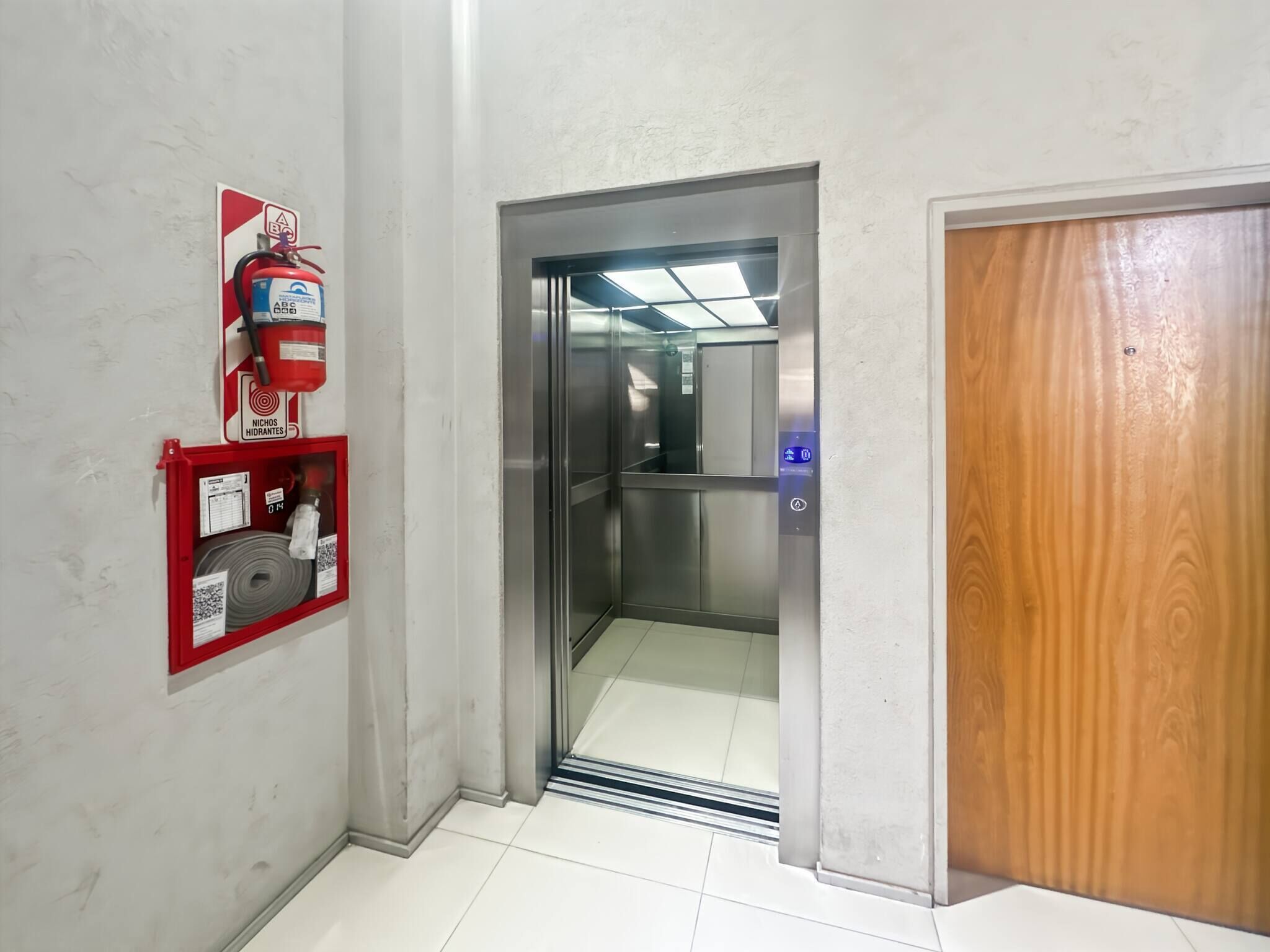 En gang med brandslukker på væggen, elevator og en trædør.