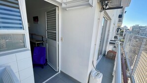 Un balcón con vistas a la ciudad, una puerta cerrada y una mesa azul.