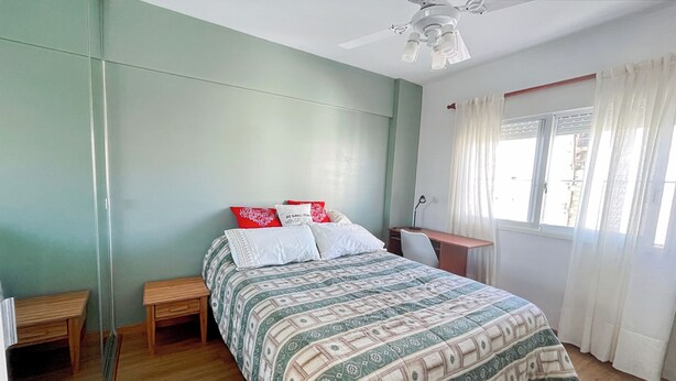 Un dormitorio con cama, escritorio, silla, lámpara de pie y ventana con cortinas.