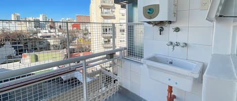 Un balcón con barandilla metálica, un lavabo blanco y un calentador de agua en la pared.