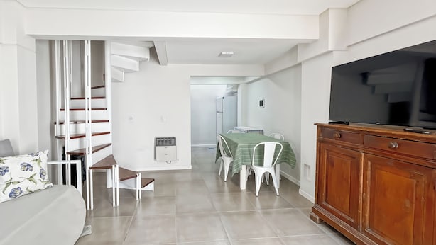 Ein modernes Wohnzimmer mit einer Couch, einem Esstisch mit Stühlen, einer Treppe und einem Fernseher auf einer Holzkommode.