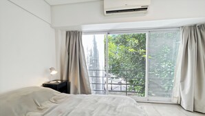 Ein Hotelzimmer mit Bett, Nachttisch, Lampe und einem Fenster mit Vorhängen.