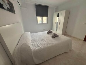 A bedroom with a bed, a window with a blind, a wardrobe, and a wall-mounted air conditioning unit. - ResbalajeHomes Granada 75 1A (Nerja)