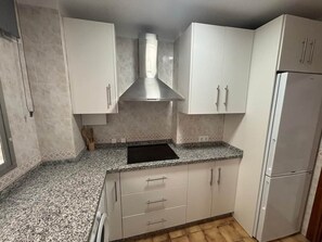 A compact kitchen with white cabinets, a stainless steel range hood, and a built-in sink. - ResbalajeHomes Granada 75 1A (Nerja)