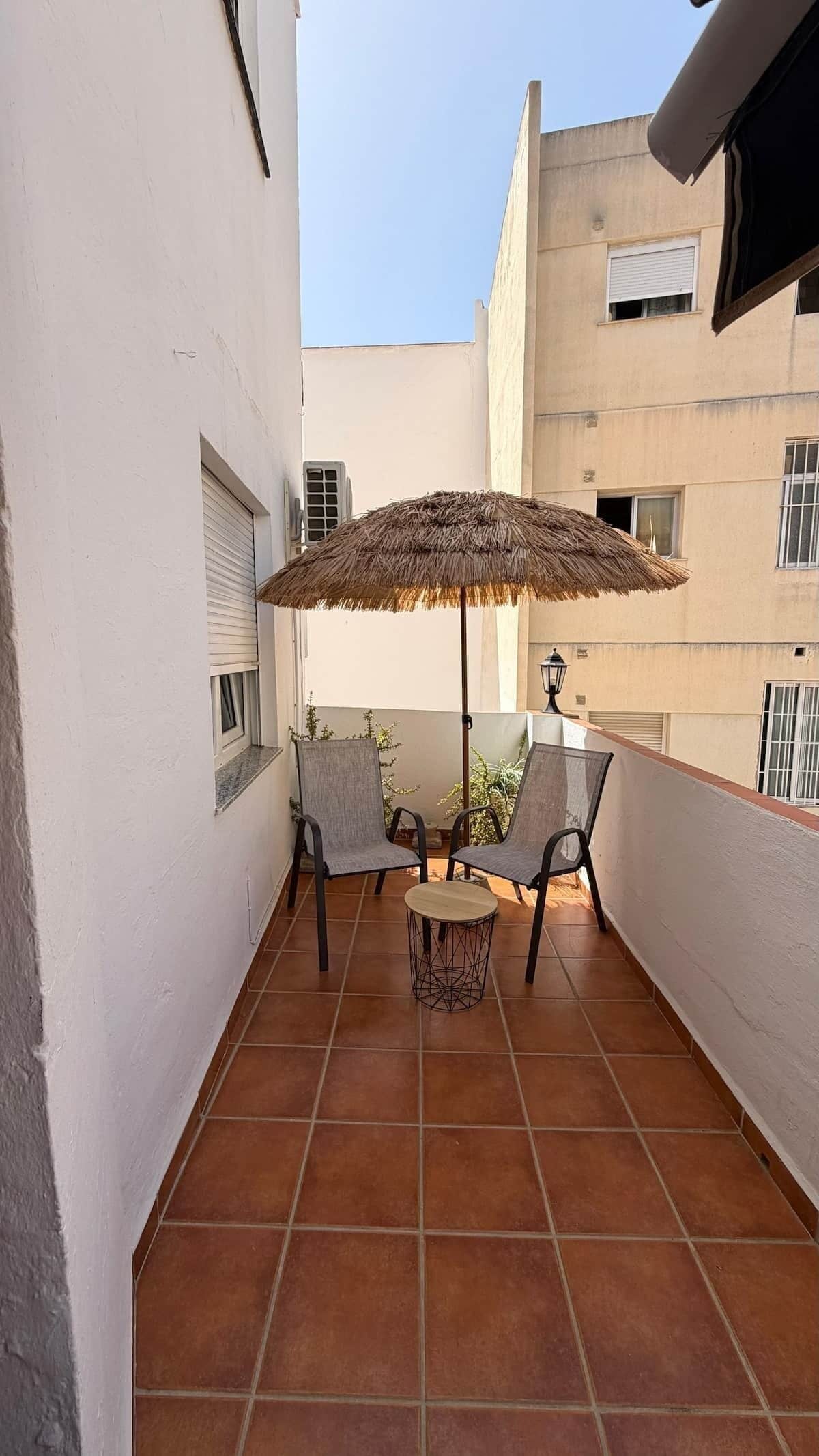 Ein Balkon mit zwei Stühlen, einem Tisch, einem Sonnenschirm und einem gefliesten Boden.