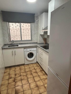 Une cuisine compacte équipée d’un lave-linge, d’un évier et d’un réfrigérateur.