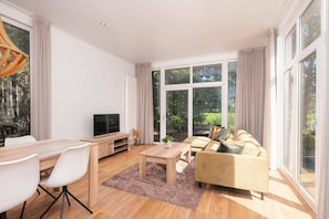A modern living room with a sofa, coffee table, TV, and dining area. - Stunning Riverside Cabin with Hot Tub (Zuna)