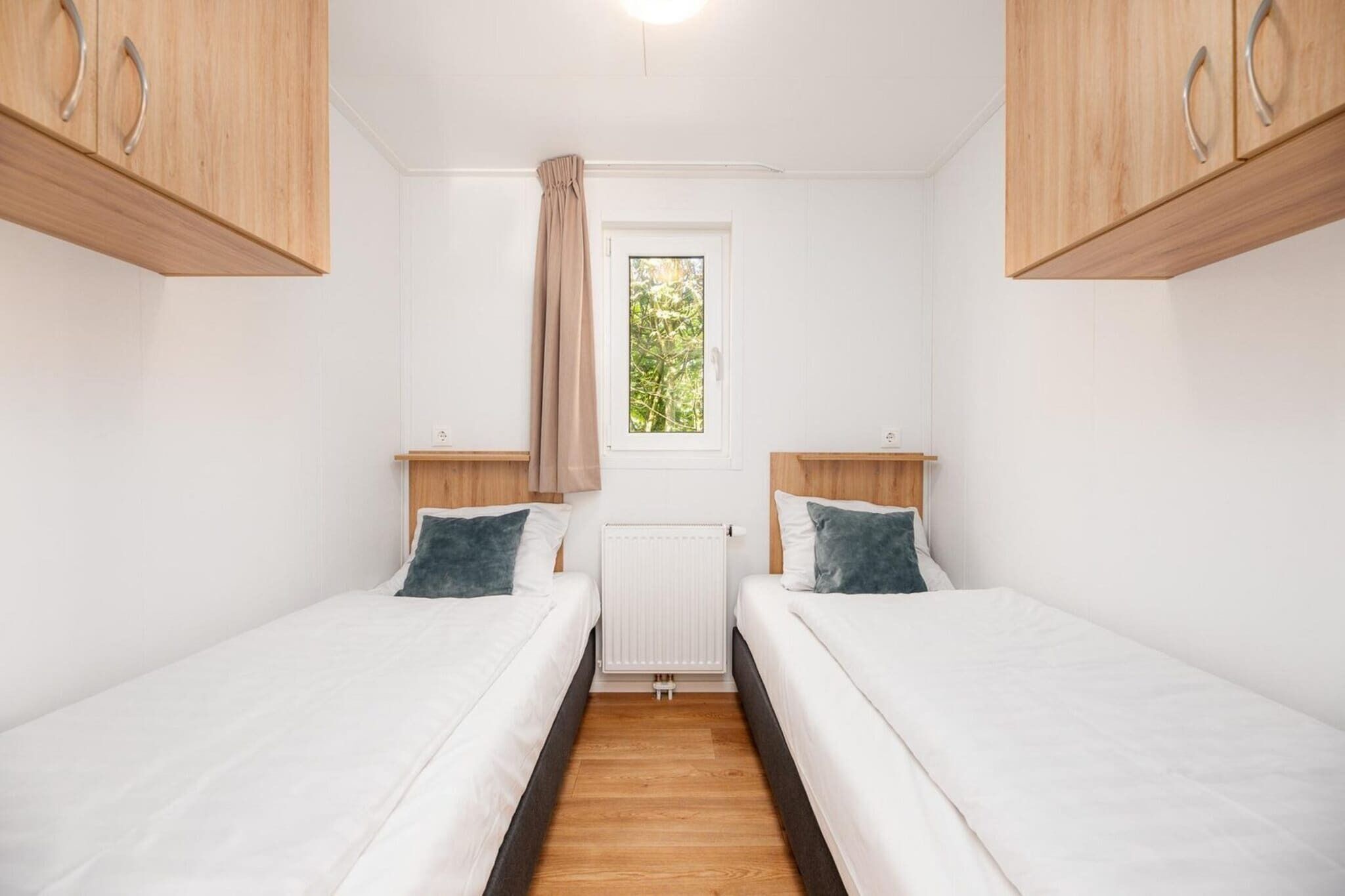Ein Zimmer mit zwei Einzelbetten, einem Fenster mit Blick auf Bäume und einer Heizung.