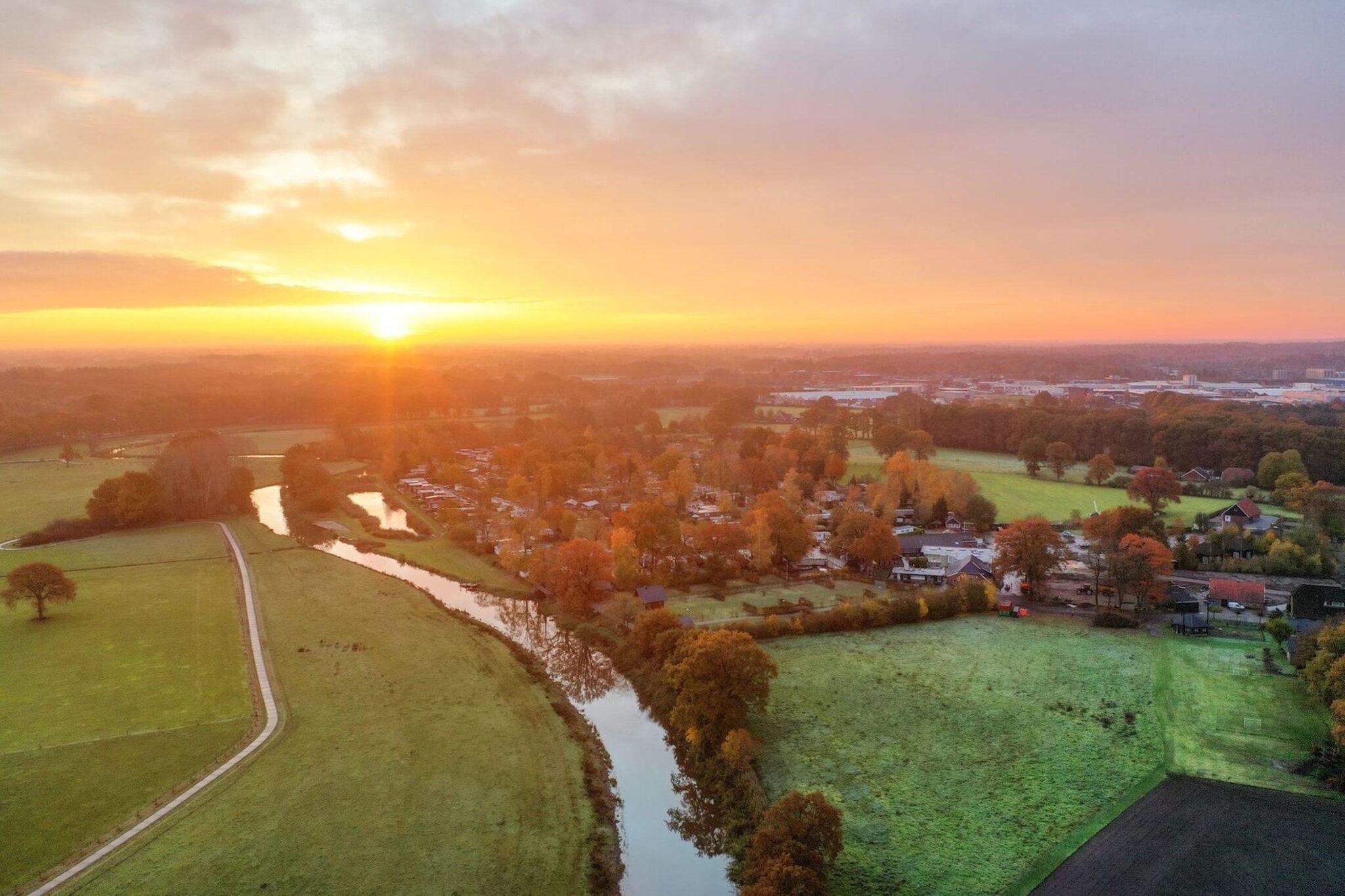 An aerial view of a rural area with fields, a river, and houses during sunset.