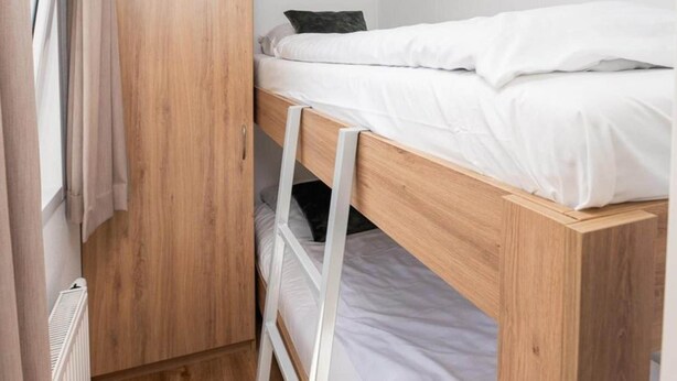 A bunk bed with a ladder, a wooden wardrobe, and a radiator.