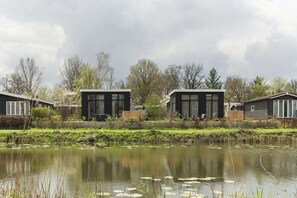 A modern residential area with two houses, a pond with lily pads, and surrounding greenery. - Stunning Riverside Cabin with Hot Tub (Zuna)