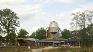 A modern observatory with a large dome, a covered walkway, and outdoor seating areas.