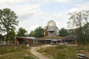 A modern observatory with a large dome, a covered walkway, and outdoor seating areas.