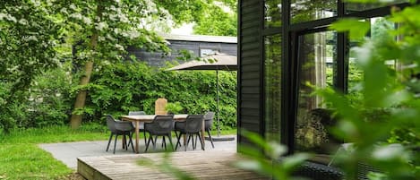 Une terrasse avec une table et des chaises, entourée de verdure et dotée d’une plateforme en bois.