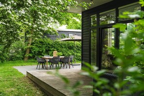 Een terras met een tafel en stoelen, omringd door groen en een houten terras.
