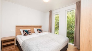 Un dormitorio con cama, dos almohadas, una mesita de noche, una ventana con cortinas y vista a la vegetación.