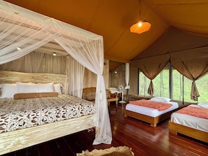 A spacious room with a large bed, two smaller beds, a wooden floor, and a ceiling fan.