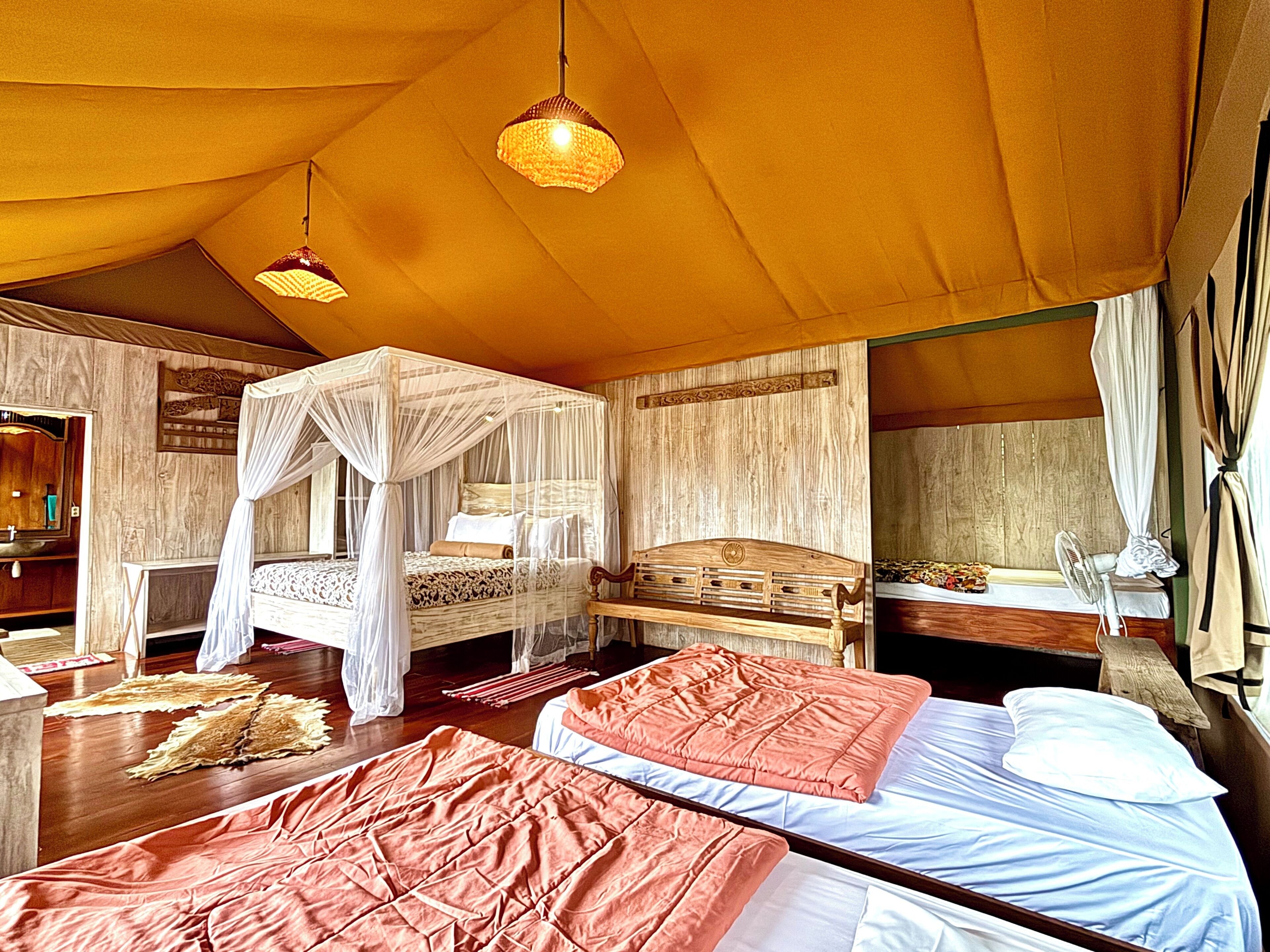Une chambre aménagée comme une tente, avec deux lits, un lit à baldaquin et un coin salon avec un banc.