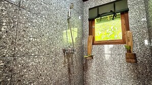 A bathroom with a granite tile wall, a shower with a hose, and a window with a view of a field.