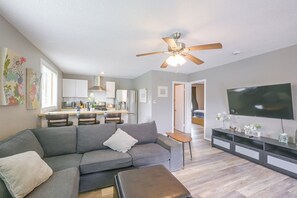Ein modernes Wohnzimmer mit grauem Sofa, Couchtisch, Fernseher und Deckenventilator.