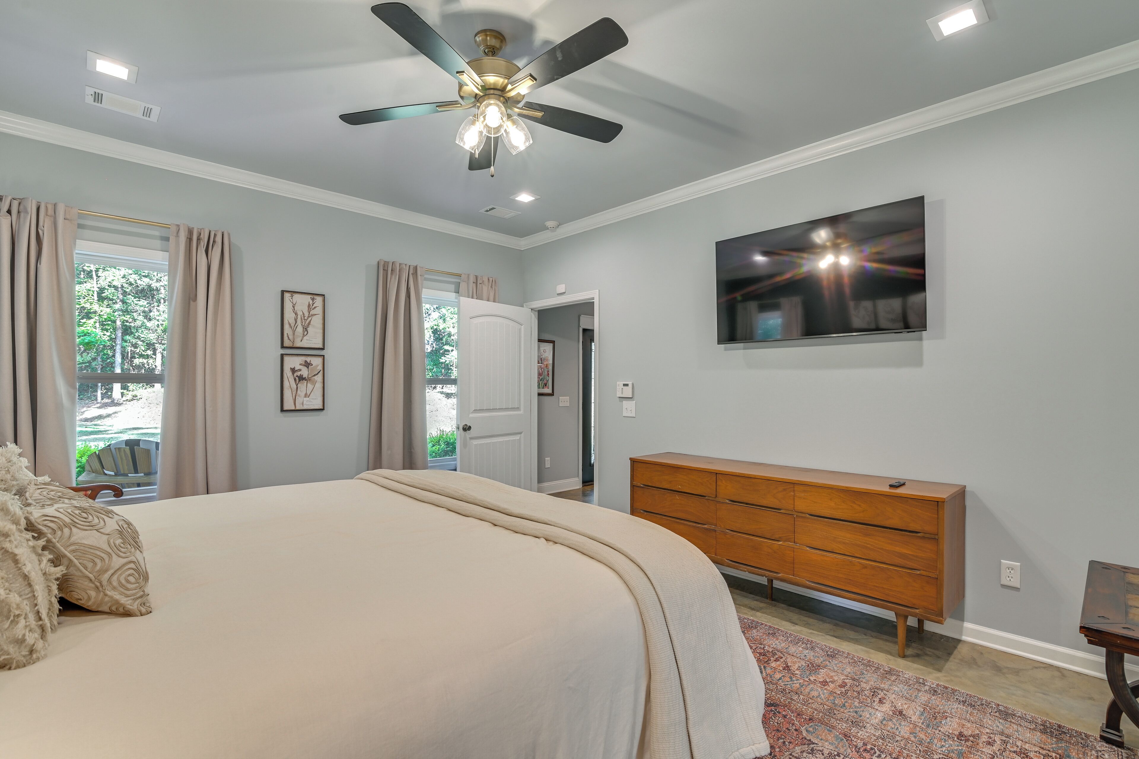 Un dormitorio con cama, ventilador de techo, cómoda, televisor y ventana con cortinas.