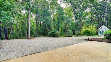 A gravel driveway leading to a house with a small garden area, surrounded by a dense forest.