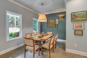 A dining area with a wooden table and chairs, a pendant light, and artwork on the wall.