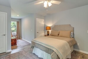 A bedroom with a bed, a nightstand, a lamp, a ceiling fan, and a view of a balcony.