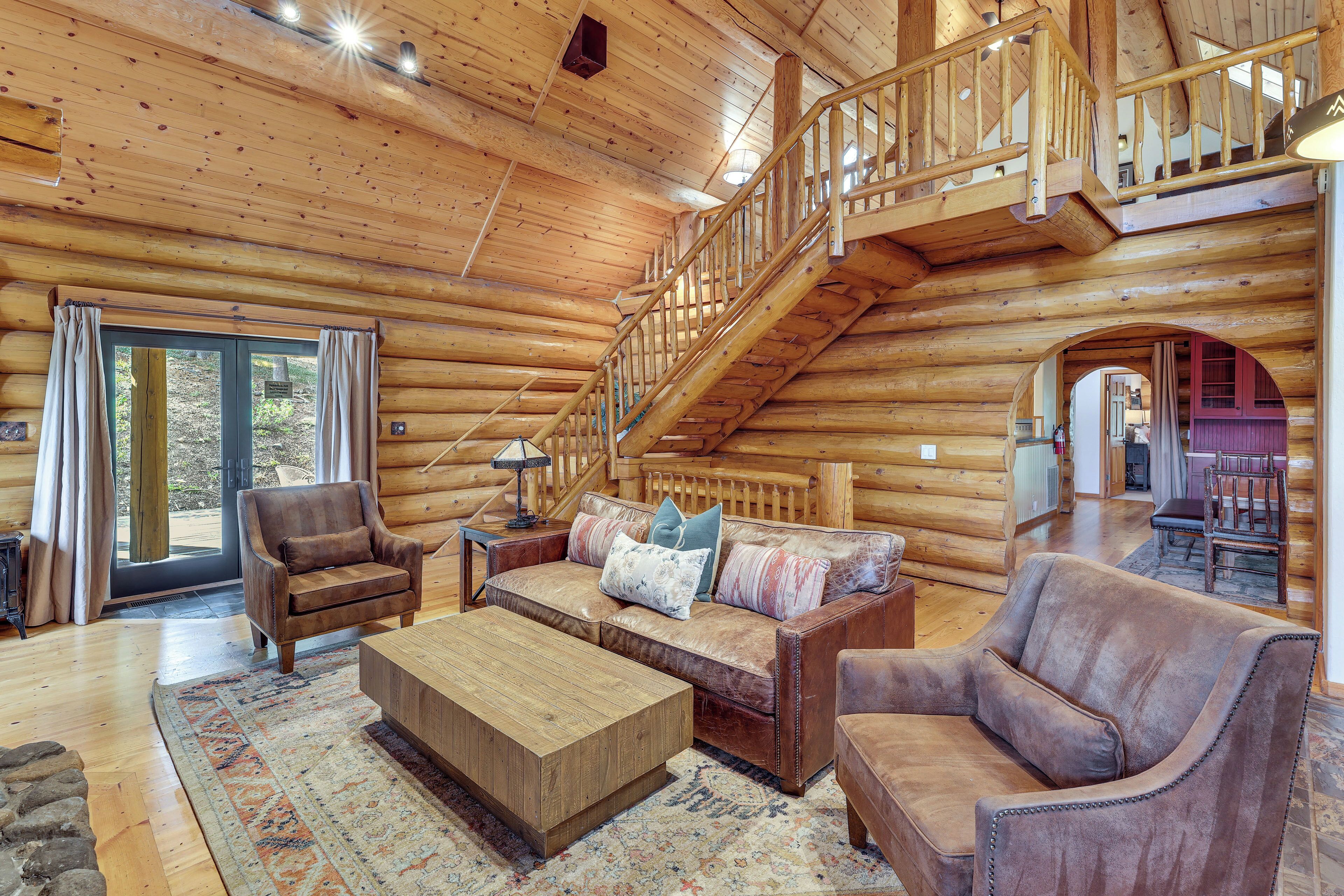 L'intérieur d'une cabane en rondins, avec un escalier en bois, des meubles en cuir et une grande fenêtre.