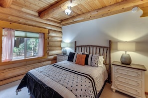 Une chambre située dans un chalet en rondins, avec un lit, des tables de chevet et une fenêtre avec des rideaux.