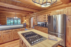 L’intérieur d’un chalet en bois comprend un espace cuisine équipé d’un réfrigérateur en acier inoxydable, d’une cuisinière à gaz, de meubles de rangement en bois et d’un lustre.
