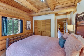A log cabin bedroom with a large bed, wooden walls, a window with curtains, and a wooden ceiling. - All-Season Family Cabin w/ Forest Views in Truckee (Truckee)