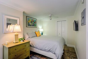 A bedroom with a bed, a dresser, a nightstand, a ceiling fan, a door, and a wall-mounted light fixture. - Prime Naples Park Location! Beachy Duplex (Naples)